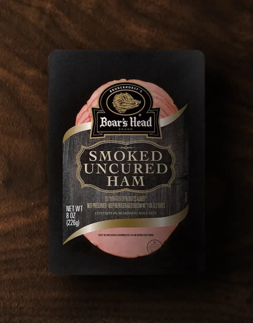 A aerial view of a package of the Boar's Head® Smoked Uncured Ham sits on a wood colored background.
