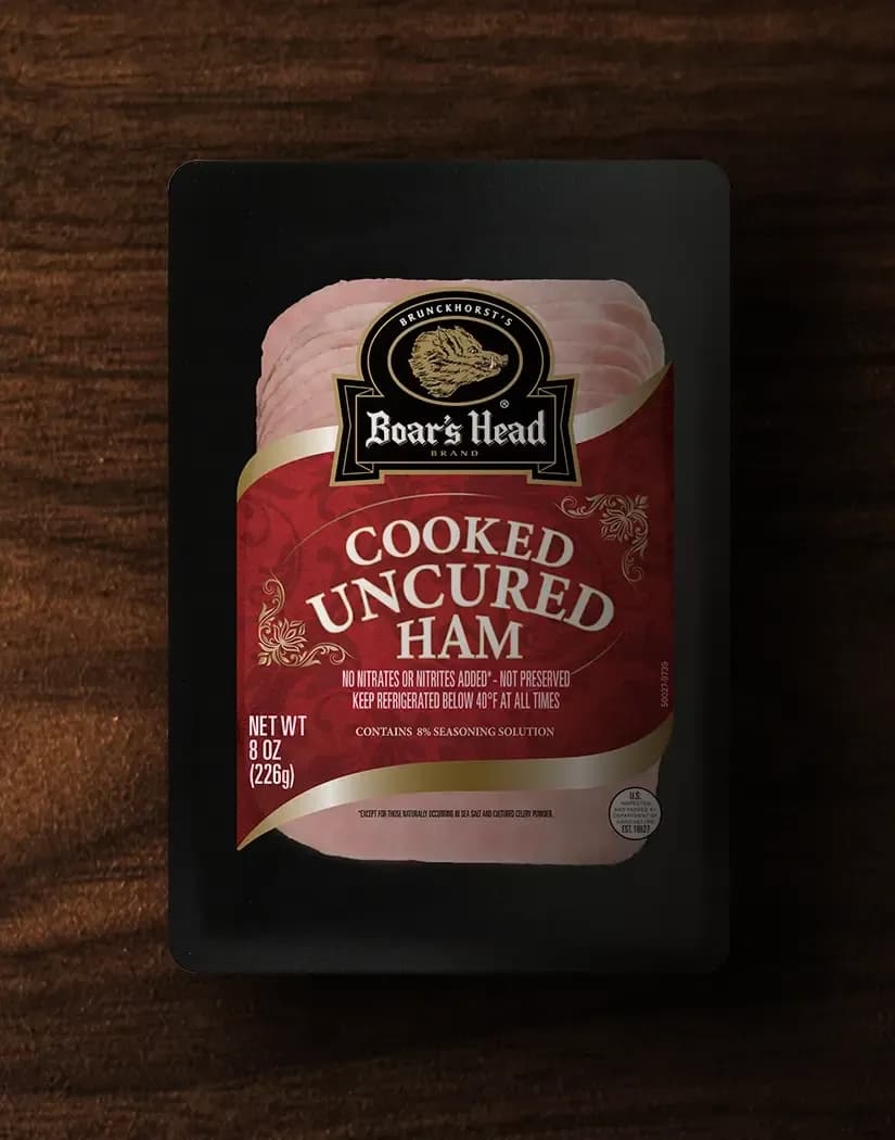 An aerial view of a package of Boar's Head® Cooked Uncured Ham sits on a wood table.