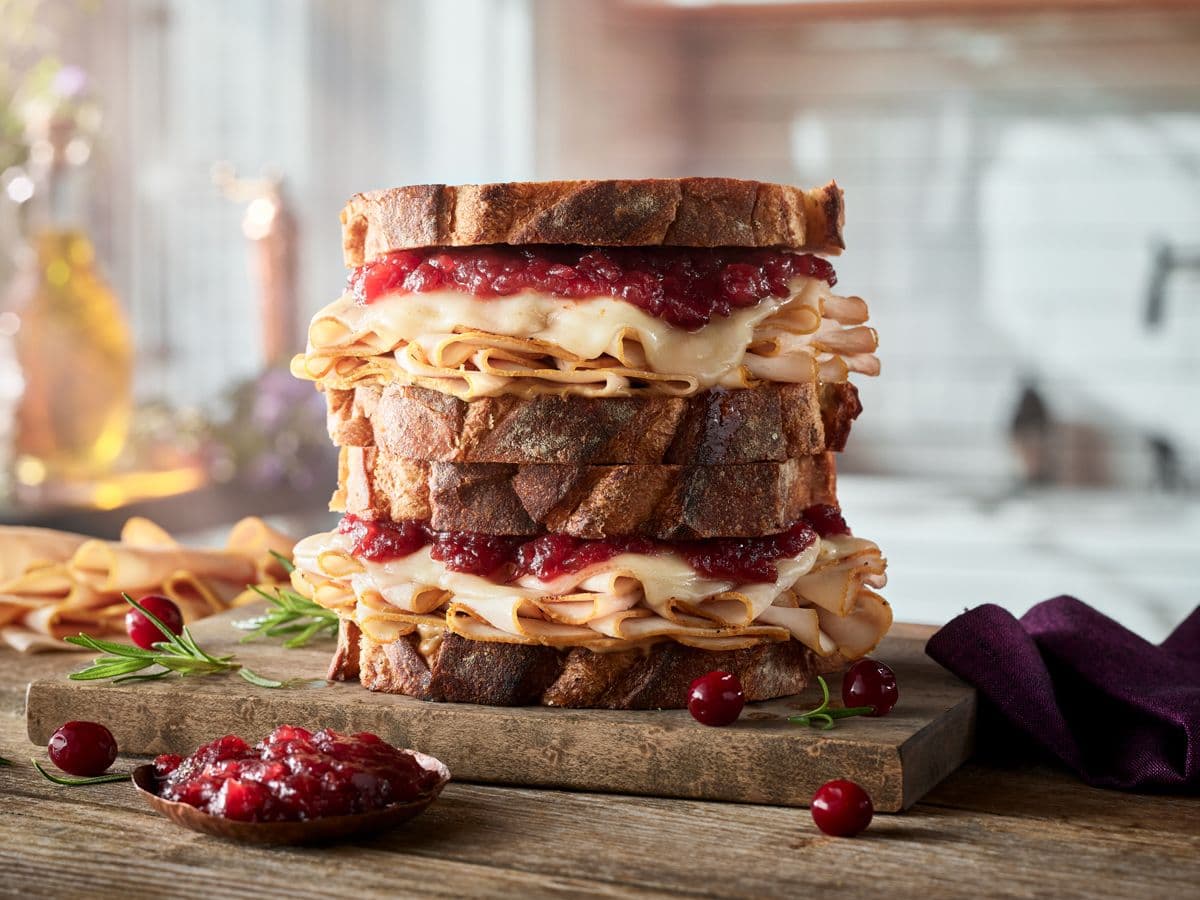 A sandwich made with Boar's Head® The Fryer's™ Deep Fried* Turkey Breast, melty cheese, cranberry sauce, and multigrain bread sits on a kitchen counter.